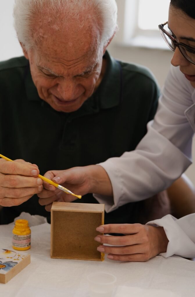 Senhor idoso a pintar uma caixa de madeira com a ajuda de uma animadora