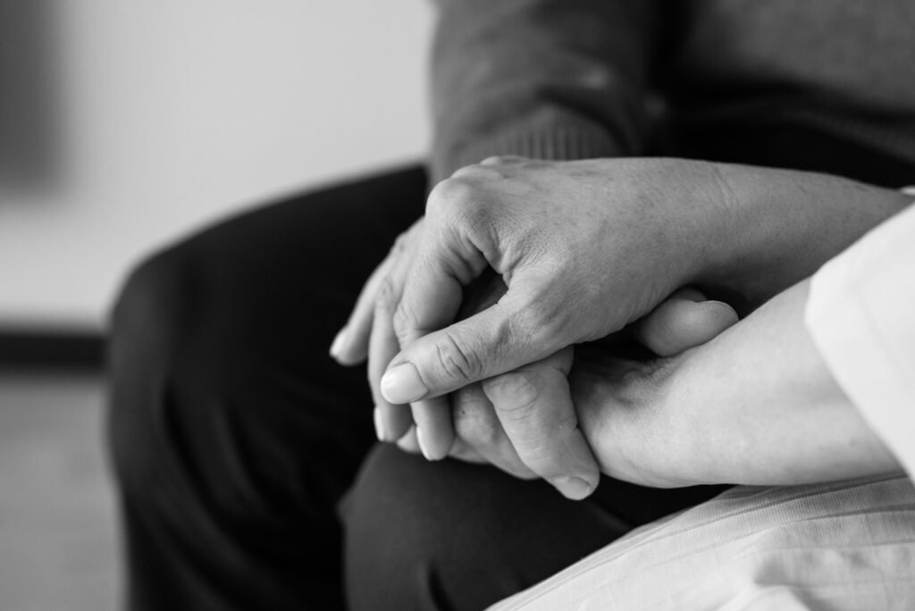 Mãos de uma cuidadora a segurar as mãos de uma pessoa idosa